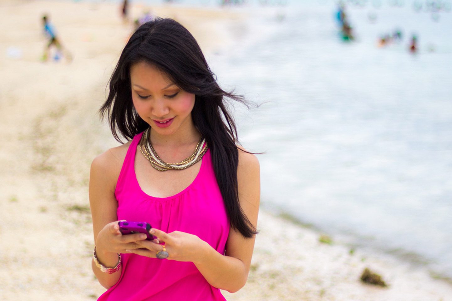 Asian woman holding cell phone and smiling on the beach